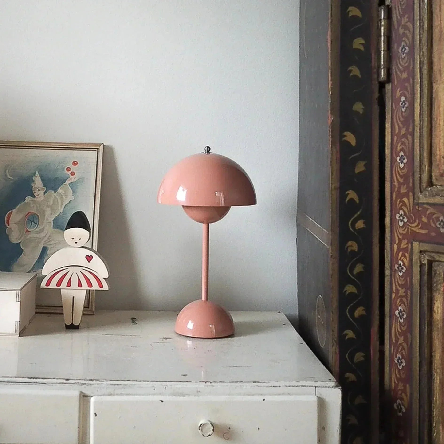 Lampe design rose poudré sur commode blanche, style moderne pour intérieur élégant, avec décoration murale et figurine.